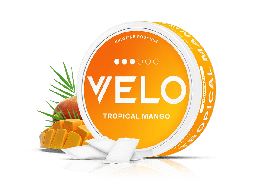 Velo Nicotine Pouches |  A round orange container labeled VELO Tropical Mango is displayed with nicotine pouches in front, alongside a sliced mango and green leaves, highlighting the vibrant allure of exotic fruit flavours against a white background.