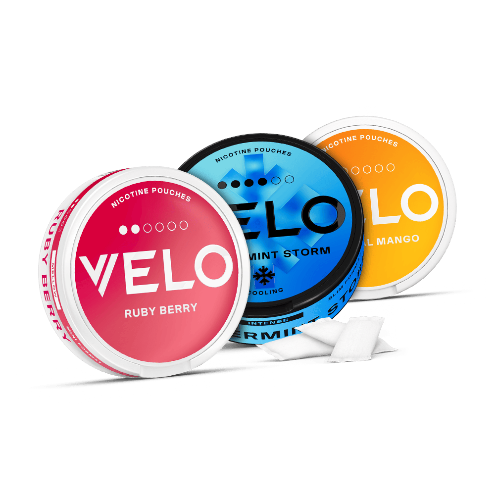 Velo Nicotine Pouches |  Three round containers of VELO nicotine pouches in Ruby Berry, Mint Storm, and Royal Mango flavors are displayed, with a few white Velo pouches placed in front of the containers.