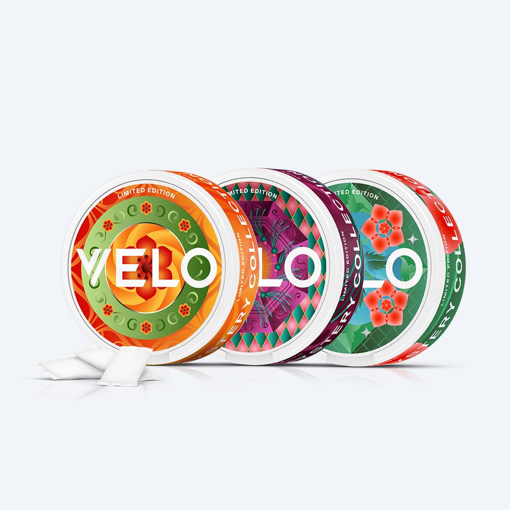 Velo Nicotine Pouches |  Three round, colorful containers of the VELO GB Mystery Collection Bundle with geometric designs, arranged side-by-side with two loose pouches in front.