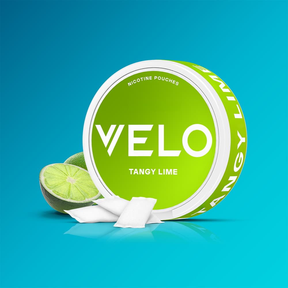 Velo Nicotine Pouches |  A round VELO Tangy Lime container is displayed with nicotine pouches arranged in front and a sliced lime nearby, all set against a blue backdrop to emphasize the zesty citrus flavour of Tangy Lime.
