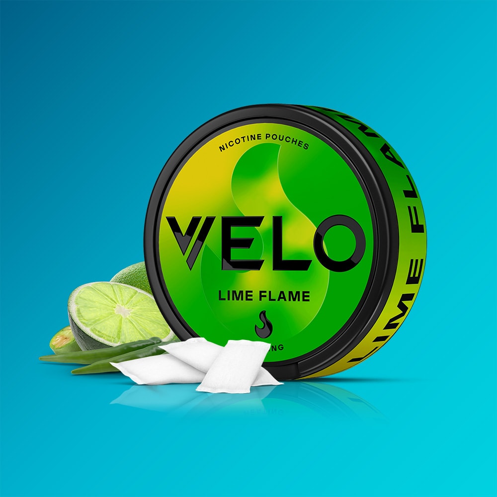 Velo Nicotine Pouches |  A round can of VELO Lime Flame nicotine pouches is displayed with sliced lime, aloe leaves, and a few white pouches on a blue background. The can features green and yellow accents with bold black text, suggesting the aromatic jalapeno twist that enhances the refreshing lime flavor.