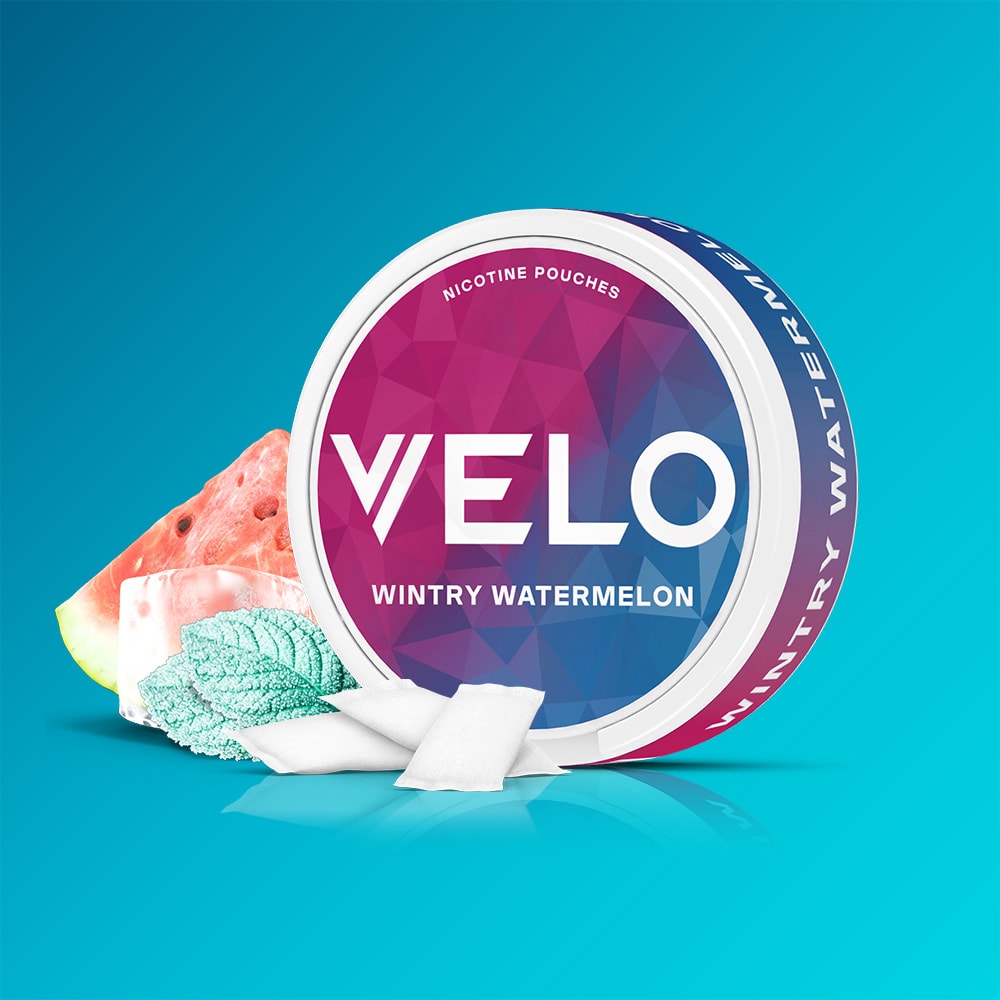 Velo Nicotine Pouches |  A VELO Wintry Watermelon container featuring nicotine pouches is showcased next to a ripe watermelon slice, ice cubes, and mint leaves atop a cool blue gradient background, highlighting the refreshing combination of watermelon and peppermint flavors.