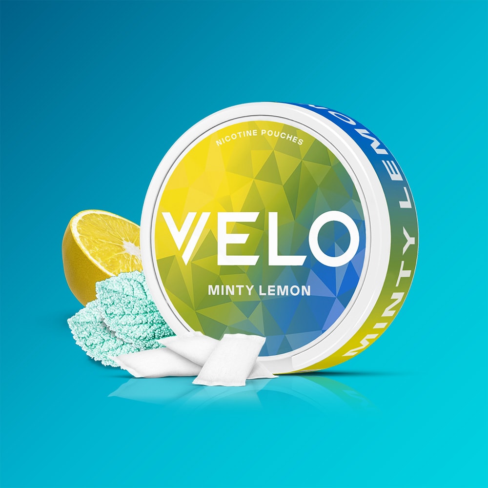 Velo Nicotine Pouches |  A round VELO Minty Lemon container rests on a blue background, accompanied by a sliced lemon and several white pouches. The packaging showcases a green and yellow geometric design that captures the refreshing flavors of lemon and peppermint.