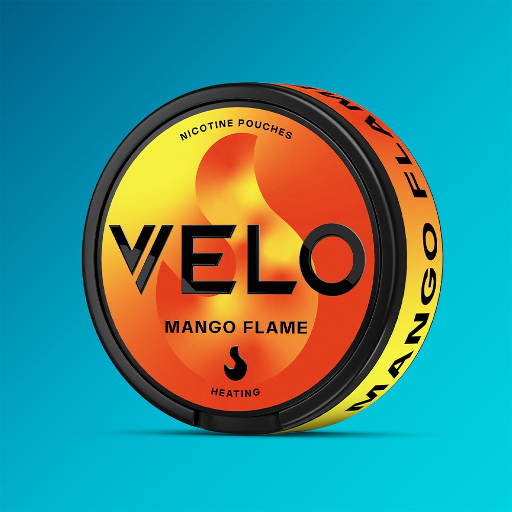 Velo Nicotine Pouches |  A round container of VELO Mango Flame nicotine pouches featuring an orange and yellow flame design set against a blue background. The label displays “Nicotine Pouches” and “Heating,” highlighting the intense burning sensation and bold heated mango flavor inside each pouch.
