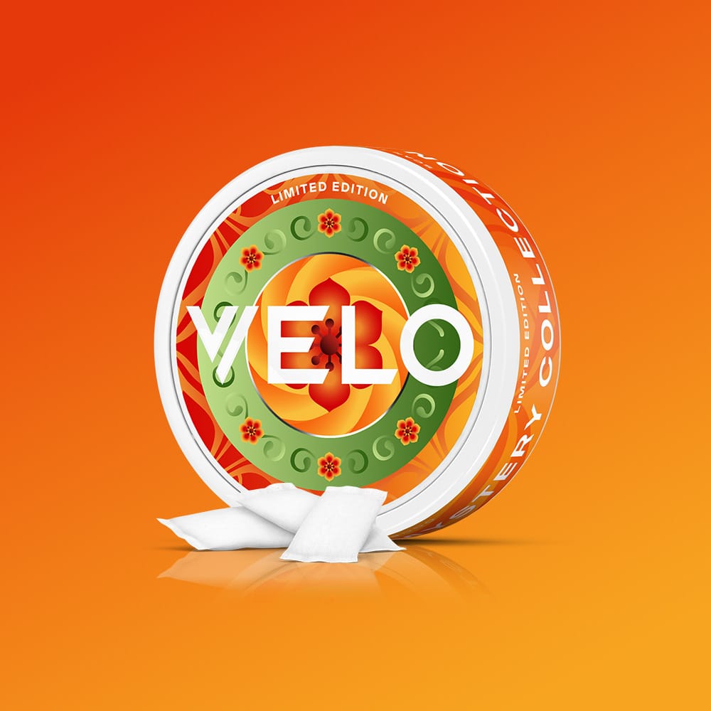 Velo Nicotine Pouches |  Round VELO GB Mystery Collection Bundle tin with an orange, red, and green patterned lid, with three small white nicotine pouches resting in front.