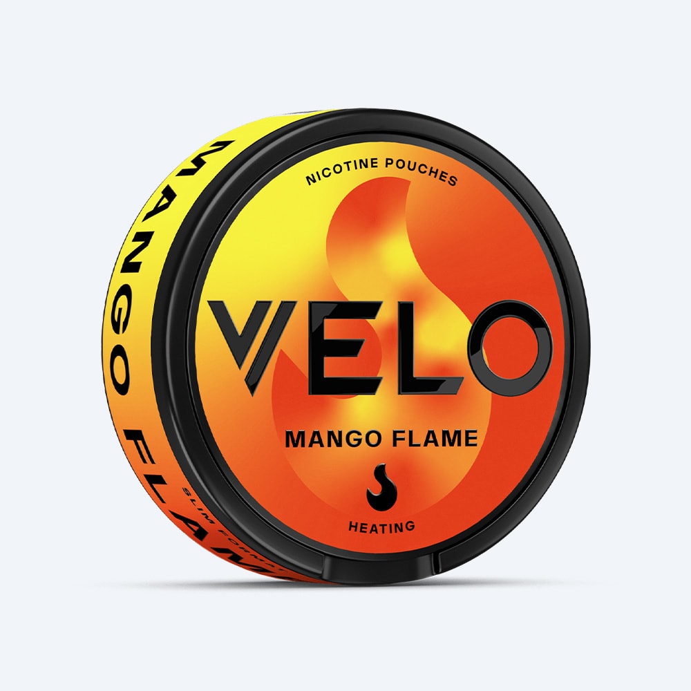 Velo Nicotine Pouches |  A black, round container of VELO Mango Flame nicotine pouches features a lid adorned with a yellow-to-orange gradient flame graphic, bold black VELO and MANGO FLAME text, a flame icon, and the words NICOTINE POUCHES and HEATING. Enjoy the taste of ripe mango combined with an intense burning sensation for a distinctively unique experience.