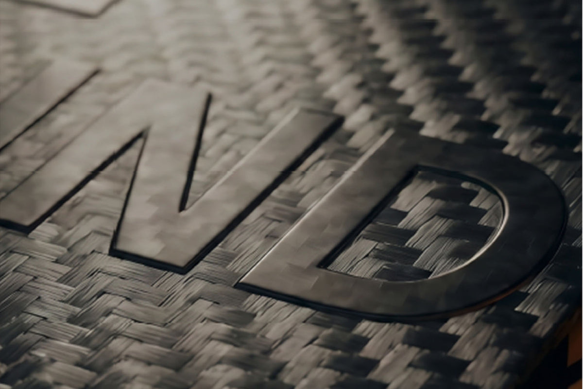 Velo Nicotine Pouches |  Close-up of black letters ND on a carbon fiber textured surface, showing intricate woven patterns and a glossy finish—evoking the sleek look of Velo nicotine pouches.