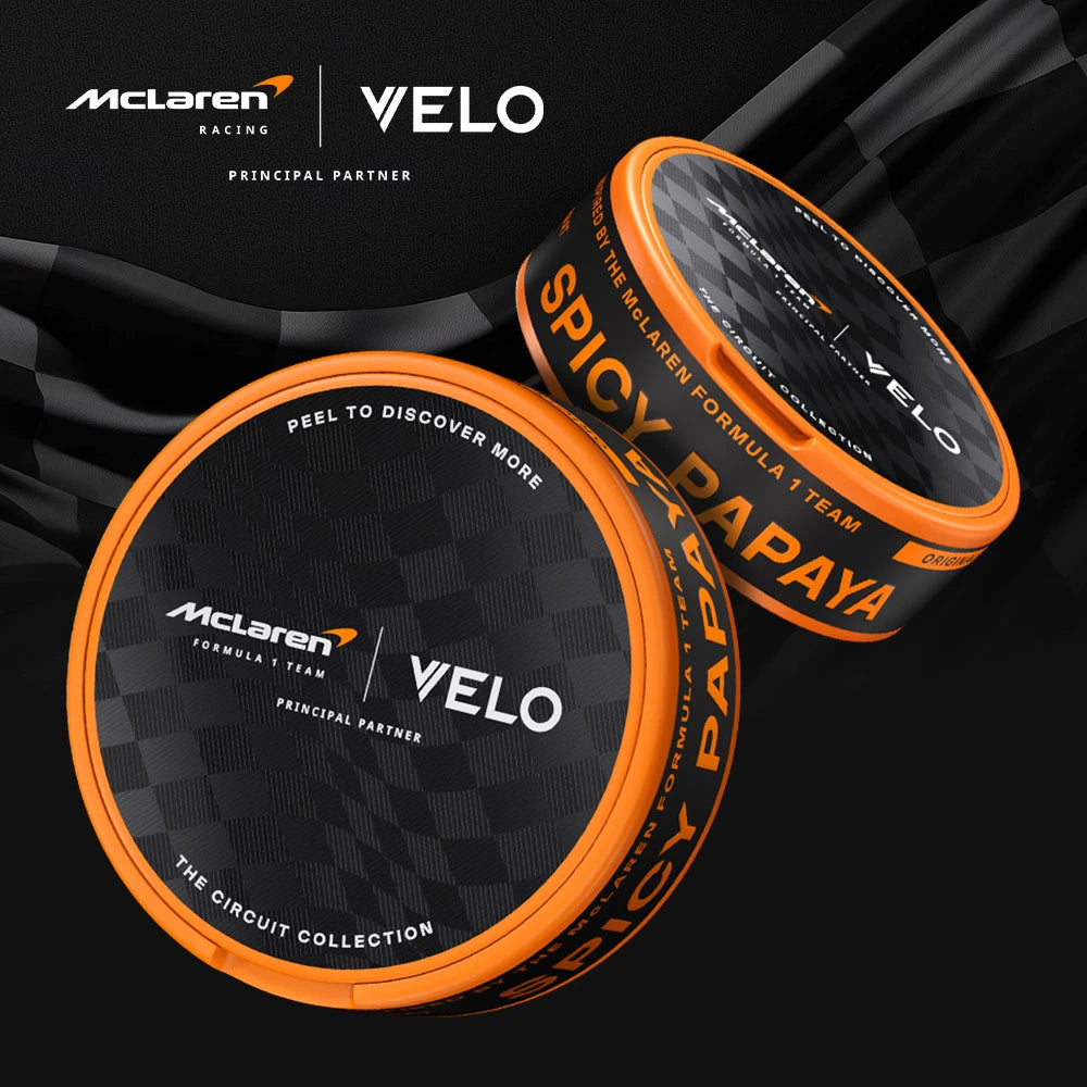 Velo Nicotine Pouches |  Two black and orange circular VELO tins with McLaren Racing branding are displayed on a dark checkered background. These sleek nicotine pouches are part of THE CIRCUIT COLLECTION, featuring the bold SPICY PAPAYA flavor.