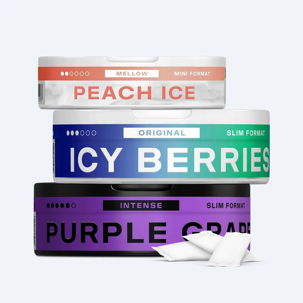 Velo Nicotine Pouches |  Three rectangular Velo cans labeled Peach Ice, Icy Berries, and Purple Grape are stacked. Two white nicotine pouches are in front of the bottom can. Each can displays its format and intensity level.