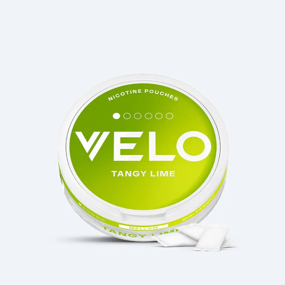 Velo Nicotine Pouches |  A round container of VELO Tangy Lime nicotine pouches with a green and white label is shown on a white background. Two white Velo pouches are placed in front of the container.