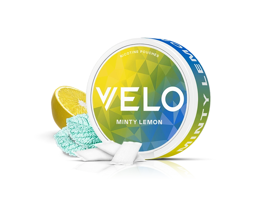 Velo Nicotine Pouches |  A round container of VELO Minty Lemon nicotine pouches is shown with a sliced lemon, blue mint powder, and several white rectangular Velo pouches in front. The background is plain white.
