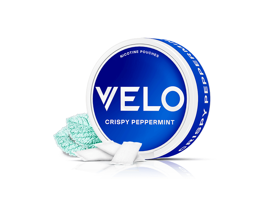Velo Nicotine Pouches |  A round blue Velo can labeled VELO CRISPY PEPPERMINT sits on a white background, with several white nicotine pouches and some aqua-colored mint crystals displayed beside it.
