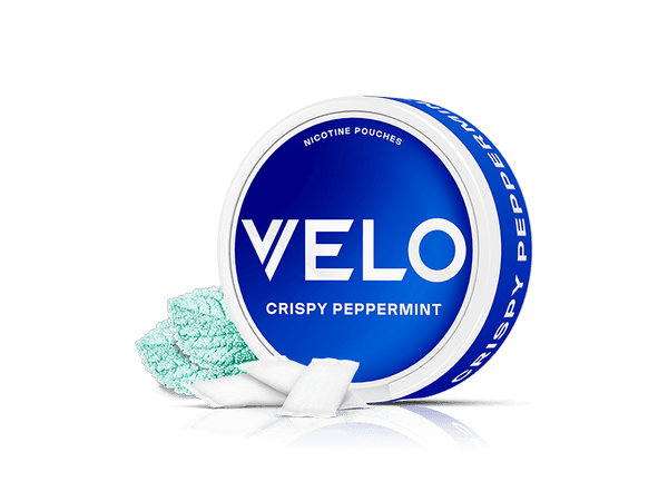 Velo Nicotine Pouches |  A round blue Velo can labeled VELO CRISPY PEPPERMINT sits on a white background, with several white nicotine pouches and some aqua-colored mint crystals displayed beside it.