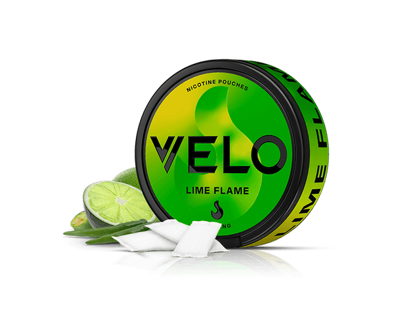 Velo Nicotine Pouches |  Round VELO Lime Flame nicotine pouches container, green and yellow with black text, is shown alongside a sliced lime, green chili, and two white nicotine pouches on a white background.