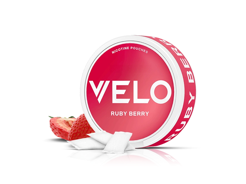 Velo Nicotine Pouches |  A round Velo Ruby Berry nicotine pouch container with a bold pink label, a sliced strawberry, and two white nicotine pouches in front, all on a white background.