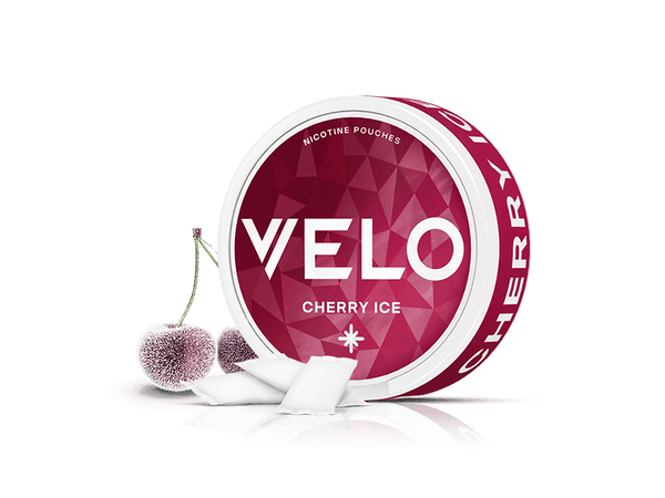 Velo Nicotine Pouches |  A round container of VELO Cherry Ice nicotine pouches stands next to two frosty cherries and several Velo pouches, all on a white background.