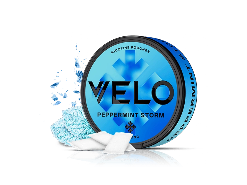 Velo Nicotine Pouches |  A blue tin of VELO Peppermint Storm nicotine pouches sits on a white background, with several Velo pouches and a sprinkle of blue powder arranged artfully beside it.
