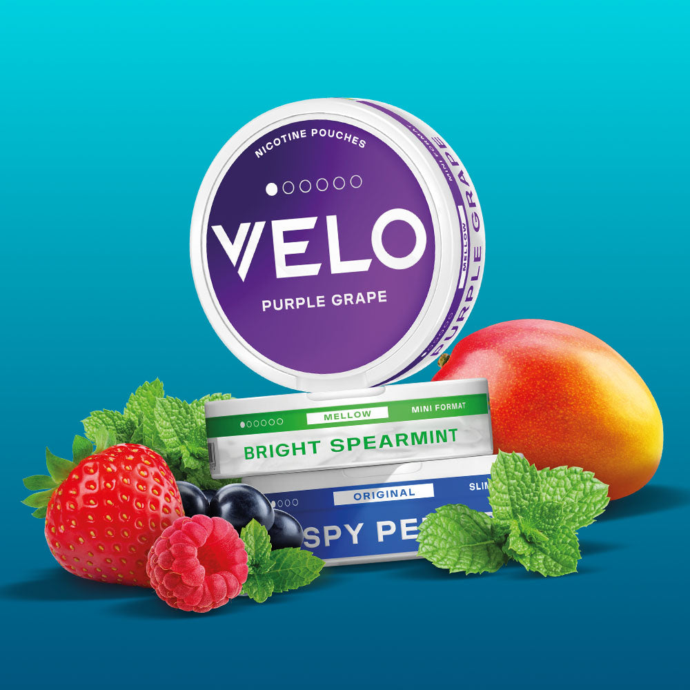 Velo Nicotine Pouches |  A stack of VELO nicotine pouches in different flavors, surrounded by a mango, strawberry, raspberry, blueberries, and mint leaves, on a blue background. Perfect for those seeking a refreshing and flavorful nicotine experience with VELO pouches.