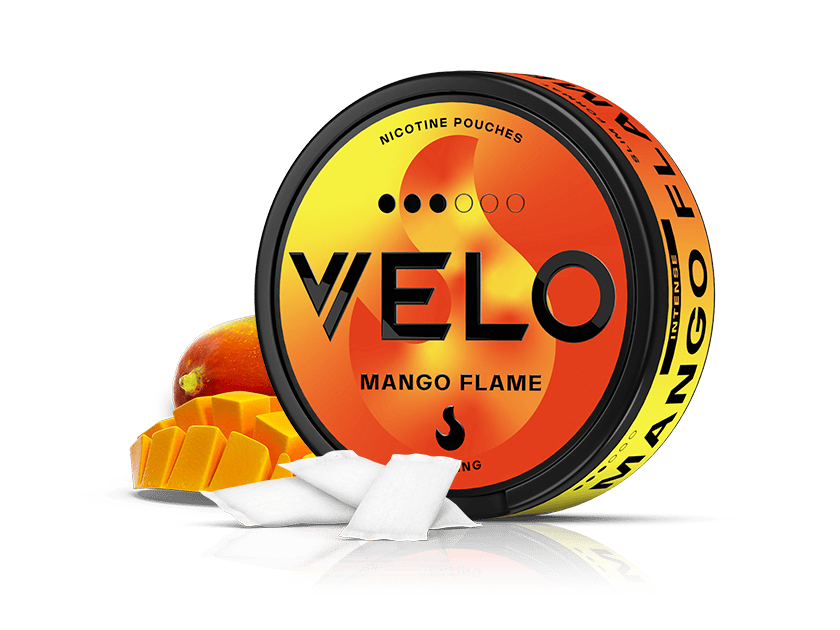 Velo Nicotine Pouches |  A round container of VELO Mango Flame sits beside a sliced mango and two white pouches, featuring vibrant orange and yellow packaging that suggests the intense heat and ripe mango flavor within.