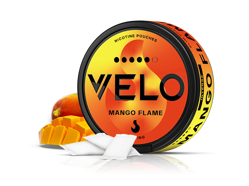 Velo Nicotine Pouches |  A round container labeled VELO Mango Flame nicotine pouches is displayed, with a sliced mango and two white pouches in front. The packaging showcases a vibrant yellow and orange gradient design, evoking the intense burning sensation and ripe mango flavors offered by each Mango Flame pouch.